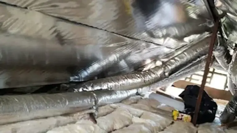 Wide-angle photograph looking up into a sun-drenched Camarillo attic showing one side with thin, compressed fiberglass b